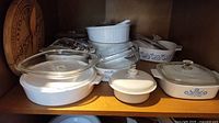 Shelf full of CorningWare Blue Cornflower casserole dishes including round and rectangular shapes with several glass lids stacked and some placed.