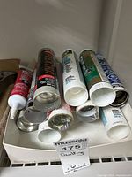 Photo shows tubes of caulking and sealant packed in a box with some tubes open and others sealed. Brands visible include Mulco, DAP, Kwik Seal.