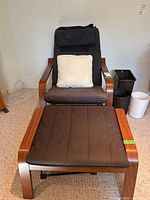 Full view of wood frame chair with dark brown upholstery, beige accent cushion on seat, and matching dark brown ottoman placed in front
