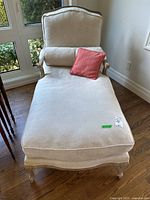 Front profile of chaise lounge showing full chaise shape with beige upholstery and coral-red pillow