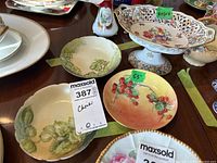 Photo of a set of small plates with botanical designs including grapes and berries, alongside a footed decorative dish with floral pattern, showing lot contents.