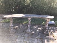Full front view of curved bench on stone patio under foliage