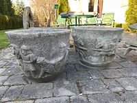 Front view showing both concrete planters with decorative reliefs of figures and horses in outdoor setting.