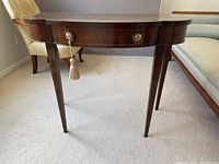 Full view of wooden console table with one drawer and tapered legs in room setting.