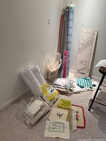 Crafting supplies including batting rolls, cushion filler in plastic bags, fabric bolts, some needlework pieces, and a large cutting board with ruler surface.