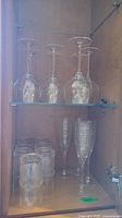 Photo of glass cabinet shelf with 4 champagne flutes, 6 stemmed wine glasses, and 6 tumblers.