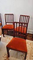 Pair of side dining chairs showing wooden slat backs and orange velvet seats