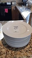 Stack of 12 white porcelain dinner plates on a kitchen granite countertop showing the top view.