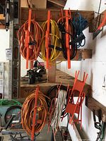 Six extension cords in various colors coiled on orange metal reel caddies mounted on wall.