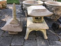 Two stone pagoda statues displayed outdoors on a paved area surrounded by large planters, showing surface wear.