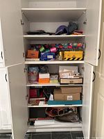 Full view of the five-shelf white cabinet filled with wrapping paper, ribbons, bows, tags, gift boxes, and packing materials.