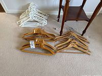 Wide view showing multiple wooden hangers with metal hooks, some wooden hangers feature black printed text with branding 'CREED', adjacent to a group of white plastic hangers stacked together.