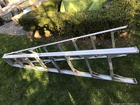 Full view of metal extension ladder laid on grass showing length and construction.