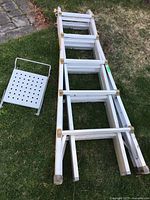 Aluminum three-section extension ladder laid on grass with removable metal platform beside it