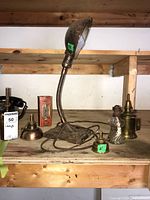 Photo showing the vintage metal adjustable desk lamp with flexible neck and several metal and glass oil lamp bases on a wooden shelf.