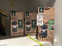 Three boxed Woods LED Rechargeable Camping Lanterns on a shelf with visible product branding and labels.