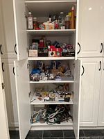 Five cabinet shelves view showing assorted light bulbs, timers, extension cords, and other household items organized in boxes and loose items.