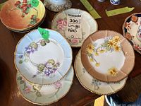 Overview photo showing the five small Limoges plates stacked and arranged on a table alongside other ceramic items, displaying varied hand-painted floral designs with gold trim.