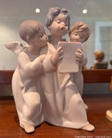 Front view of porcelain figurine showing three angels, one holding a music book.