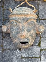 Front view of terracotta mask showing overall facial features, open mouth, and hanging rope.