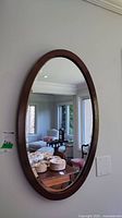 Front view of the wall mounted oval mirror reflecting parts of a living room with furniture and décor.