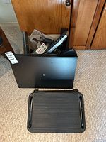 Photo of black metal desk turntable and black ribbed plastic under desk footrest on carpet in front of wooden cabinet