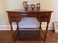 Front view of desk showing rectangular top, turned legs, five drawers and round knobs