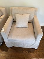 Front view of beige linen armchair with throw cushion on hardwood floor