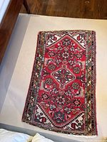 Full view of the small rectangular wool rug showing its red patterned center with white and multicolor detailing.