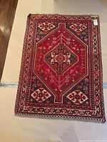 Full view of wool rug with geometric and floral patterns using red, black and cream shades, showing overall condition and pattern details.