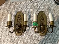 Pair of brass wall sconces with two arms each placed on carpet, showing overall condition and structure.