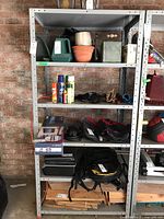 Frontal view of shelving unit with assorted garage items on shelves including watering cans, pots, spray cans, and tool bags.