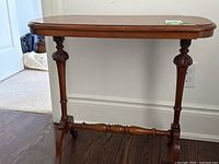 Front view of medium brown wooden side table with turned legs and stretcher base on dark hardwood floor next to wall.