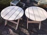 Two round white wooden side tables with slatted top viewed from above, showing weathered white paint and outdoor setting.