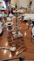 Silver plate 3-arm candelabra, six napkin rings, ornate spoon and tongs on wooden table