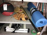Photo showing basketball, Rawlings baseball mitt, Louisville Slugger bat, and camping pad on a shelf