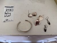 Photo of sterling silver cuff bracelet and three pairs of sterling silver earrings on white surface.
