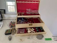 Jewelry box open showing the interior compartments containing various costume jewelry pieces including colorful beads, a pearl-like beaded necklace, some pins, and plastic baggies with jewelry pieces.