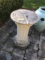Outdoor stone sundial on a fluted pedestal base with Roman numeral dial and compass rose decoration, showing weather wear and moss growth.