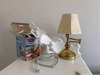 Photo showing the brass table lamp with beige embroidered shade and two white tabletop fans on a white table.