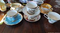 Photo of assorted varied teacups and saucers featuring floral and scenic decoration patterns, all placed on a table