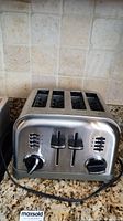 Front view of the stainless steel toaster showing four slots, dual control levers and dials.