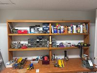 Wide view of wooden shelves with assorted hardware and tools including boxes with screws, spray cans, and locking clamps.