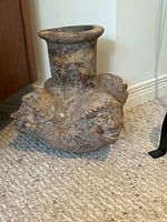 Full side view of ceramic vase showing base with multiple gargoyle-style sculpted faces and tall neck.