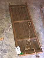 Full length view of vintage wooden sled showing slatted wood base and rope attached for pulling.