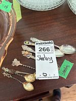 Eight vintage sterling silver souvenir spoons arranged on a wooden surface showing a variety of decorative handles and twisted stems.