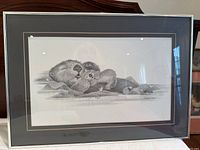 Full view of the framed charcoal drawing showing two sea otters resting, matted and framed in metallic silver.