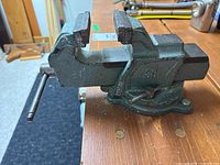 Side view of metal vise showing jaws and handle, mounted on wooden surface.