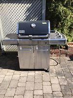 Full front view of Weber Genesis grill showing lid, control panel, griddle side shelf, storage cabinet and wheels.