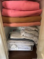 Four folded wool blankets stacked in a closet with white bedding and mattress protector beneath.